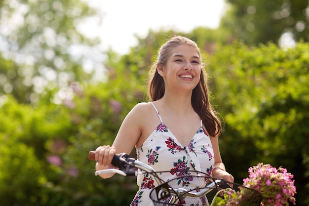 Menschen, Freizeit und Lebensstil - glückliche junge Hipster-Frau in Sommerkleidung fährt Fixie-Fahrrad mit Wildblumen im Korb im Park