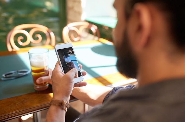 Foto menschen-, freizeit- und technologiekonzept - nahaufnahme eines mannes mit smartphone, der bier in einer bar oder kneipe fotografiert