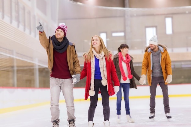 menschen, freundschaft, sport, gesten und freizeitkonzept - glückliche freunde, die mit dem finger auf die eisbahn zeigen