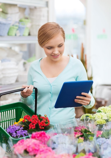 menschen, gartenarbeit, einkaufen, verkauf und konsumkonzept - glückliche frau mit tablet-pc-computer und korb, die blumen im blumenladen auswählt und kauft