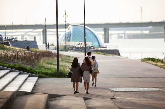 Menschen gehen an einem sonnigen Tag auf der Promenade entlang des Flusses