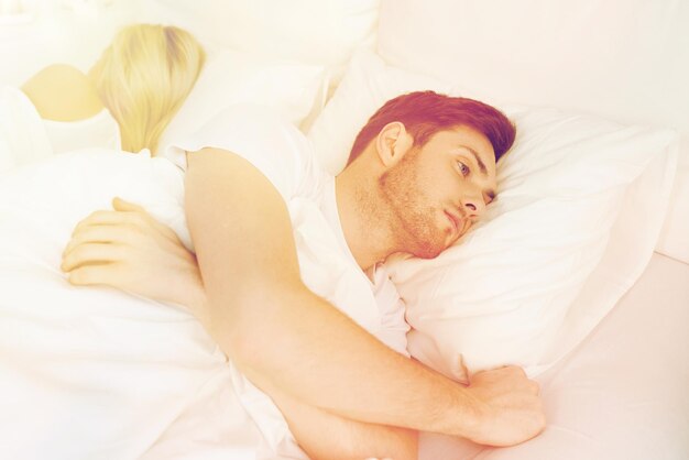 Menschen, Gesundheit, Schlafstörungskonzept - Paar, das zu Hause Rücken an Rücken im Bett liegt, und junger Mann, der an Schlaflosigkeit leidet