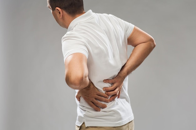 Menschen, Gesundheitsversorgung und Problemkonzept - Nahaufnahme eines Mannes, der an Rückenschmerzen oder Zügeln leidet, auf grauem Hintergrund