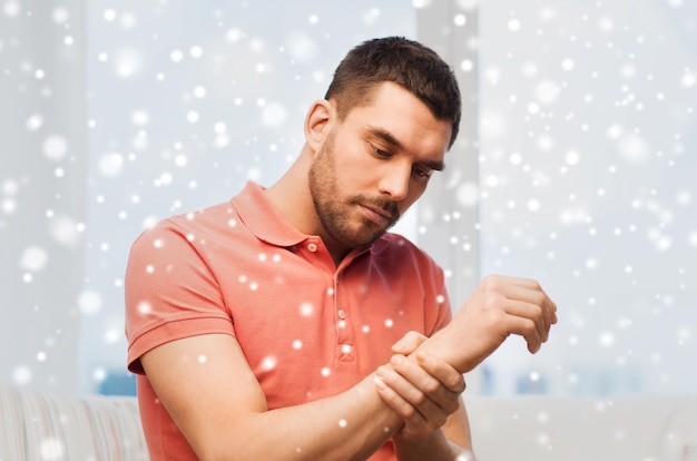 Foto menschen, gesundheitsversorgung und problemkonzept - unglücklicher mann, der zu hause über schnee unter schmerzen in der hand leidet