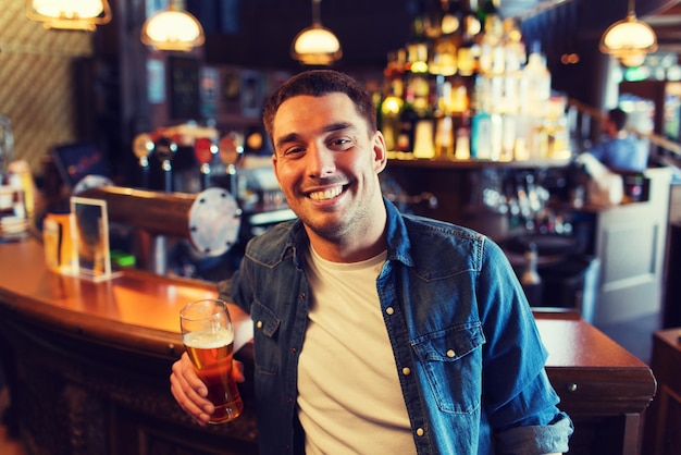 menschen, getränke, alkohol und freizeitkonzept - glücklicher junger mann, der bier in der bar oder im pub trinkt