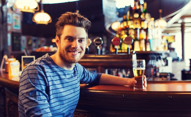 Foto menschen, getränke, alkohol und freizeitkonzept - glücklicher junger mann, der bier in der bar oder im pub trinkt