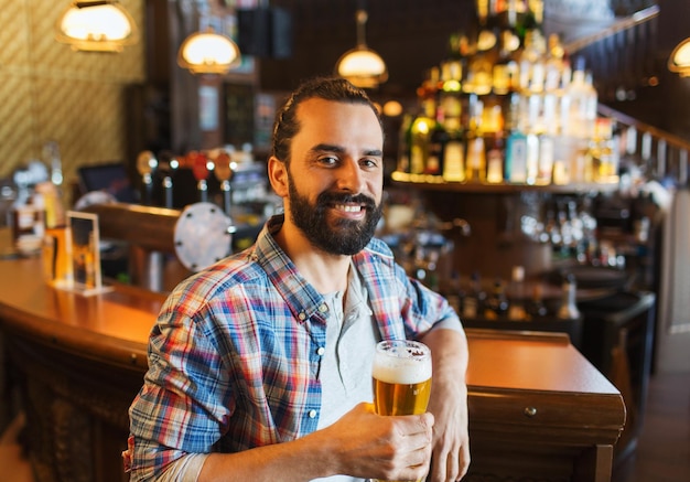 menschen, getränke, alkohol und freizeitkonzept - glücklicher junger mann, der bier in der bar oder im pub trinkt