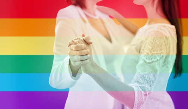 Menschen, Homosexualität, gleichgeschlechtliche Ehe und Liebeskonzept - Nahaufnahme eines glücklich verheirateten lesbischen Paares, das über Regenbogenfahnenstreifenhintergrund tanzt