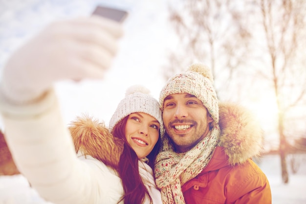 Menschen, Jahreszeit, Liebe, Technologie und Freizeitkonzept - glückliches Paar, das Selfie per Smartphone über Winterhintergrund macht