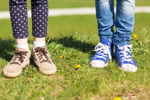 menschen, kinder, freunde und freundschaftskonzept - nahaufnahme von kinderbeinen in schuhen auf gras im freien