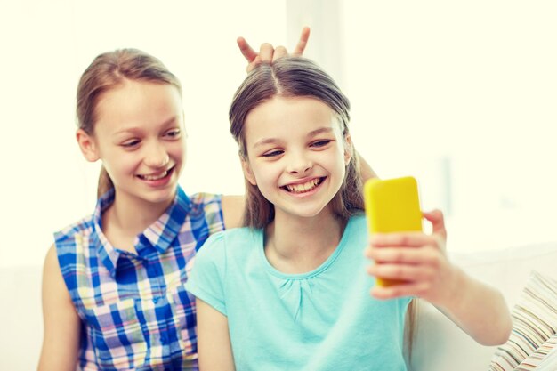 menschen, kinder, technik, freunde und freundschaftskonzept - glückliche kleine mädchen, die selfie mit dem smartphone machen und zu hause spaß haben