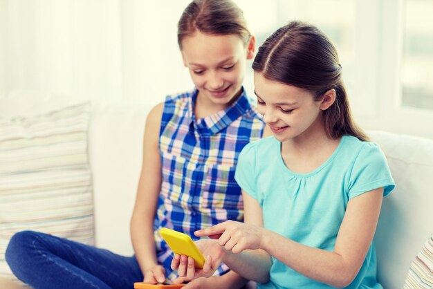 menschen, kinder, technik, freunde und freundschaftskonzept - glückliche kleine mädchen mit smartphones, die zu hause auf dem sofa sitzen