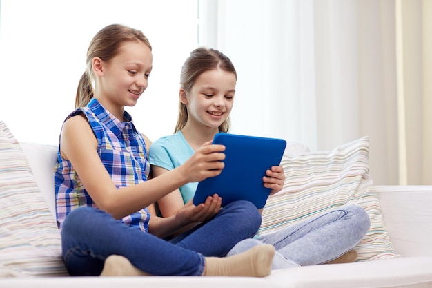 menschen, kinder, technik, freunde und freundschaftskonzept - glückliche kleine mädchen mit tablet-pc-computer, die zu hause auf dem sofa sitzen