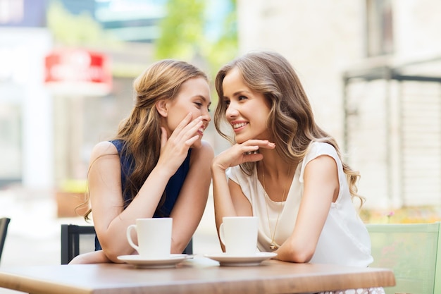 menschen-, kommunikations- und freundschaftskonzept - lächelnde junge frauen, die kaffee oder tee trinken und im café im freien klatschen