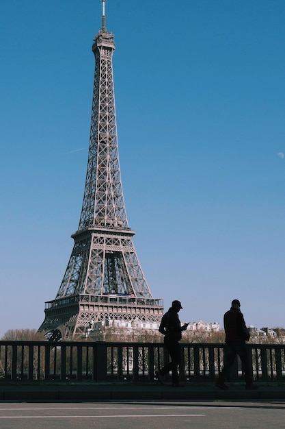 Menschen laufen am Eiffelturm vor einem klaren blauen Himmel