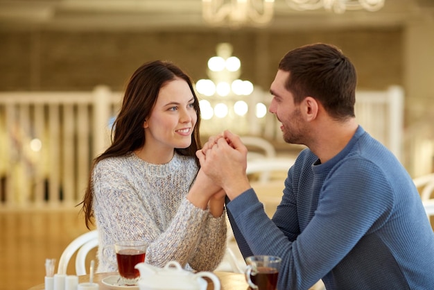 Menschen, Liebe, Romantik und Dating-Konzept - glückliches Paar, das Tee trinkt und sich im Café oder Restaurant an den Händen hält