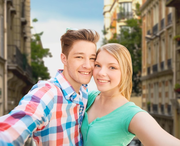 menschen, liebe, urlaub, technologie und sommerkonzept - glückliches paar, das selfie mit smartphone oder kamera über stadtstraßenhintergrund macht