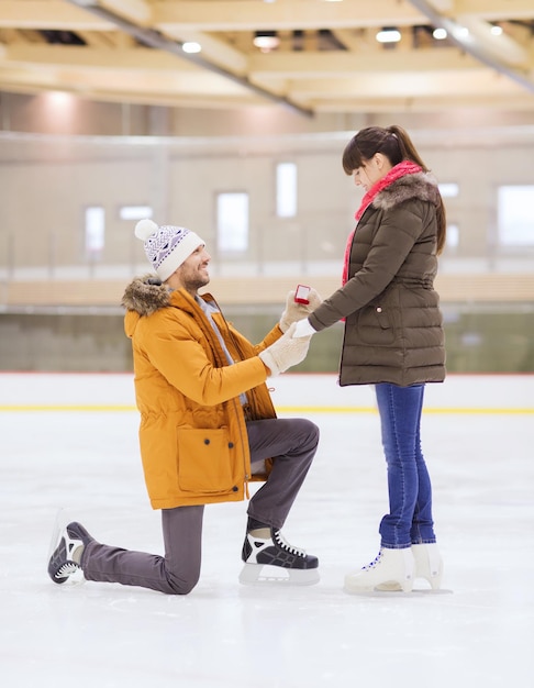 menschen, liebe, vorschlag, sport- und freizeitkonzept - glückliches paar mit verlobungsring auf eisbahn