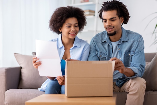 Menschen, Lieferung und Konsumkonzept - glückliches Paar mit Paketkasten und Papierformular nach Hause