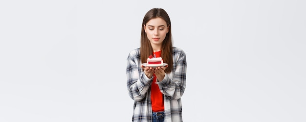 Menschen Lifestyle Urlaub und Feier Emotionen Konzept Verträumte attraktive Geburtstagskind Frau feiert bday machen Wunsch Blick auf brennende Kerze auf Kuchen weißen Hintergrund