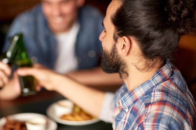 menschen, männer, freizeit, freundschaft und feierkonzept - glückliche männliche freunde, die bier trinken und flaschen an der bar oder im pub klirren