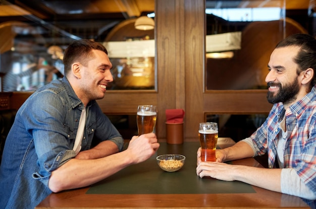 menschen, männer, freizeit, freundschaft und kommunikationskonzept - glückliche männliche freunde, die gezapftes bier in der bar oder im pub trinken