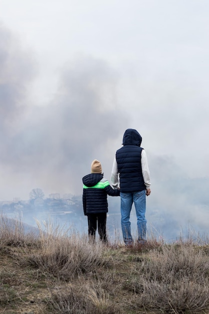 Menschen, Mann und Kind, Zeugen von Feuer in der Natur, Menschen auf einem Hügel vor dem Hintergrund einer rauchigen Atmosphäre