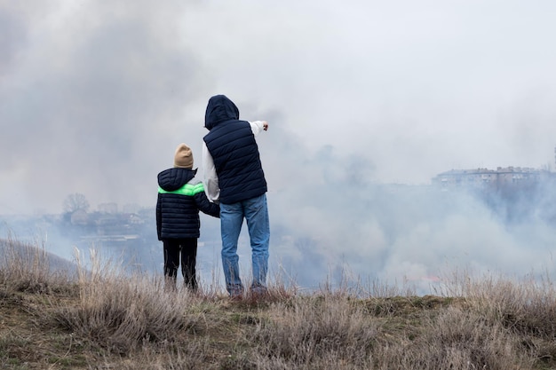 Menschen, Mann und Kind, Zeugen von Feuer in der Natur, Menschen auf einem Hügel vor dem Hintergrund einer rauchigen Atmosphäre