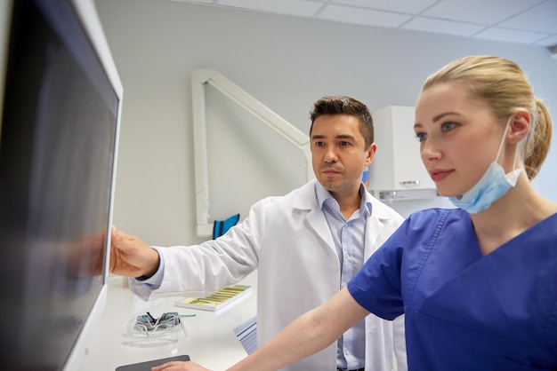 Foto menschen, medizin, stomatologie, technologie und gesundheitskonzept - zahnärzte, die in der zahnklinik einen röntgenscan auf dem monitor durchführen möchten