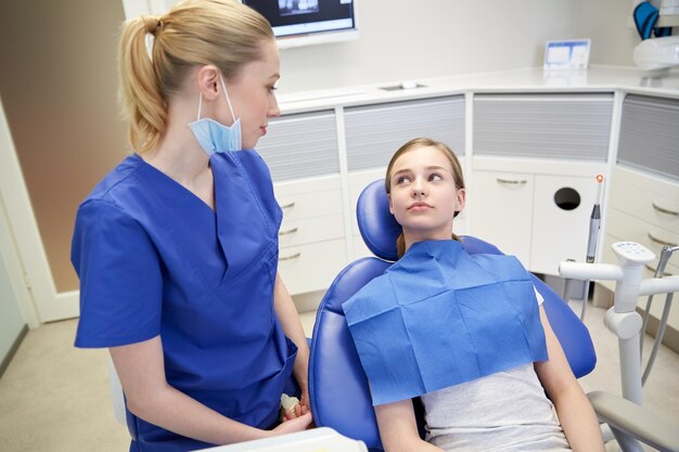 menschen, medizin, stomatologie und gesundheitskonzept - glückliche zahnärztin mit geduldigem mädchen, das im büro der zahnklinik spricht