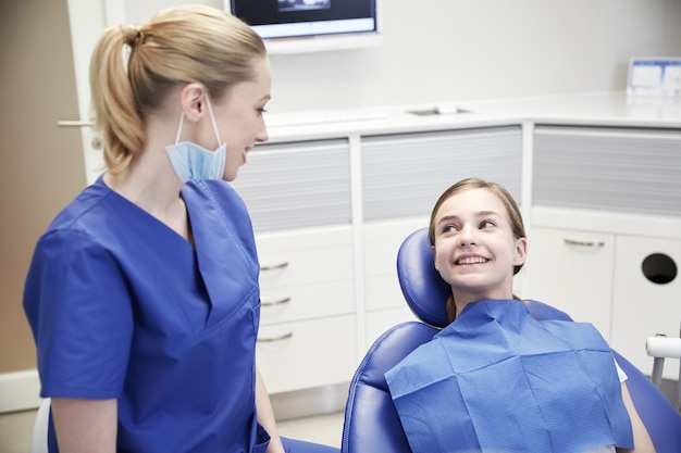 menschen, medizin, stomatologie und gesundheitskonzept - glückliche zahnärztin mit geduldigem mädchen, das im büro der zahnklinik spricht