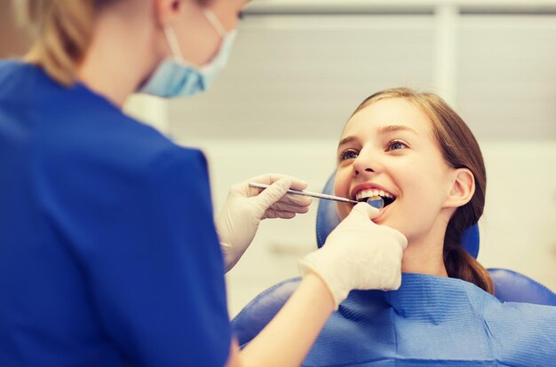menschen, medizin, stomatologie und gesundheitskonzept - glückliche zahnärztin mit spiegel, die die zähne der patientin im büro der zahnklinik überprüft