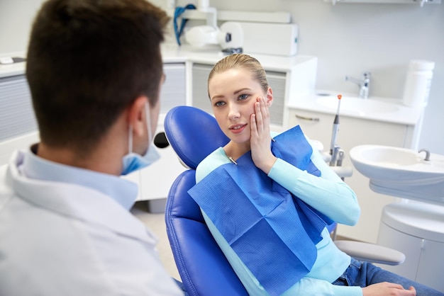 menschen, medizin, stomatologie und gesundheitskonzept - patientin, die mit einem männlichen zahnarzt spricht und sich über zahnschmerzen in der zahnklinik beschwert