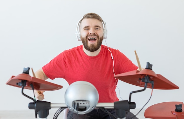 Menschen-, Musik- und Hobbykonzept - Mann mit weißen Kopfhörern, die Schlagzeug auf hellem Hintergrund spielen.