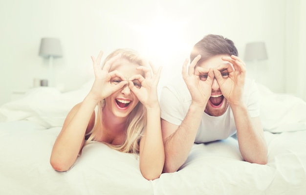 Menschen, Ruhe, Liebe, Beziehungen und Spaß Konzept - glückliches Paar liegt zu Hause im Bett und macht Fingerbrillen