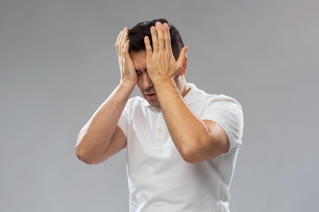 Menschen-, Schmerz- und Stresskonzept - unglücklicher Mann, der unter Kopfschmerzen leidet und seine Stirn und Augen auf grauem Hintergrund berührt