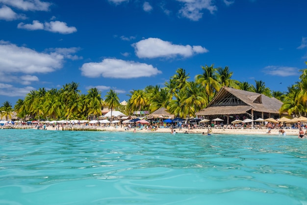 Menschen Sonnenbaden am weißen Sandstrand mit Sonnenschirmen Bungalow Bar und Kokospalmen türkisfarbene Karibik Isla Mujeres Insel Karibik Cancun Yucatan Mexiko