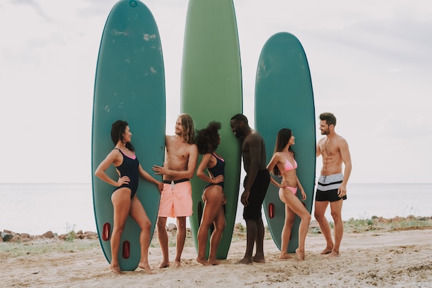 Menschen stehen am Strand hält Surfs Mädchen in Badeanzügen