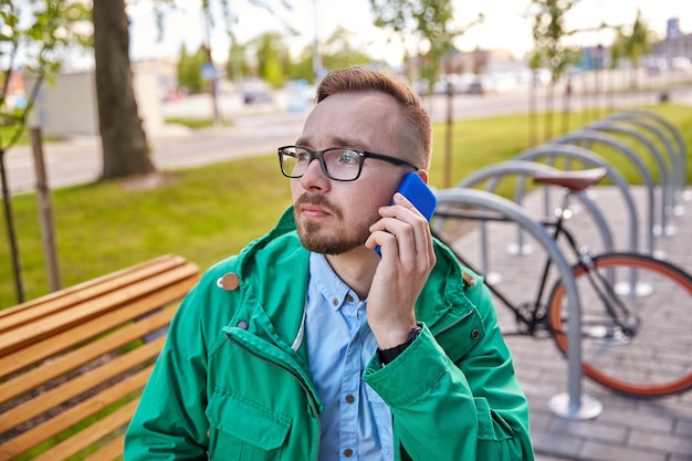 Menschen, Stil, Technologie und Lifestyle - junger Hipster-Mann mit Smartphone und Fixie-Fahrrad, der auf einer Bank in der Stadt sitzt