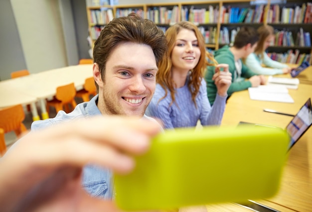 menschen, technologie, bildung und schulkonzept - glückliche schüler oder freunde mit smartphone, die selfie in der bibliothek machen