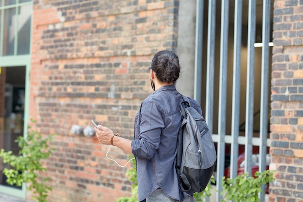 Menschen, Technologie, Reisen und Tourismus – Mann mit Rucksack, Smartphone und Kopfhörern, der die Stadtstraße entlang läuft und Musik hört