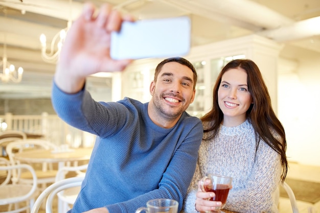 Menschen, Technologie und Dating-Konzept - glückliches Paar, das Smartphone-Selfie macht und Tee im Café oder Restaurant trinkt