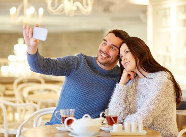Menschen, Technologie und Dating-Konzept - glückliches Paar, das Smartphone-Selfie macht und Tee im Café oder Restaurant trinkt