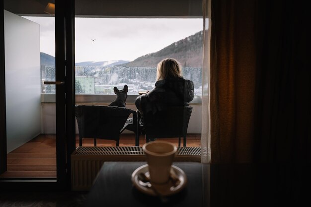 Menschen und ein französischer Bulldog sitzen auf einem Balkon mit Glasfenster