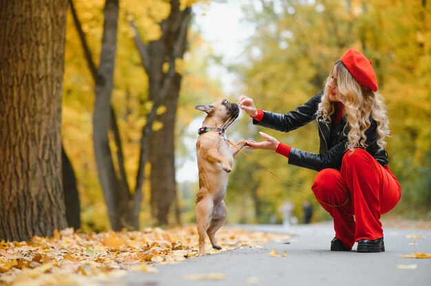 Menschen und Hunde im Freien. Schöne und glückliche Frau, die im Herbstpark mit ihrer entzückenden französischen Bulldogge spazieren geht.