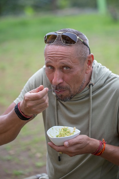 Menschen und Lifestyle-Konzept. Glücklicher Mann mittleren Alters, der eine Avocado-Guacamole in der Natur isst, Nahaufnahme Porträt