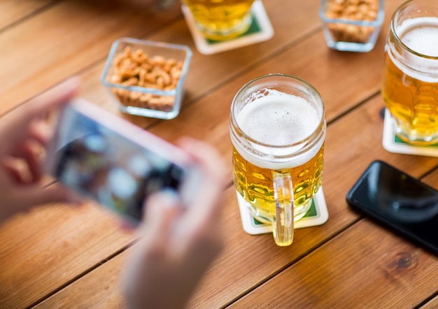 Menschen- und Technologiekonzept - Nahaufnahme von Händen mit Smartphone, das Bier an der Bar darstellt