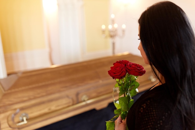 Menschen und Trauerkonzept - Frau mit roten Rosen und Sarg bei einer Beerdigung in der Kirche