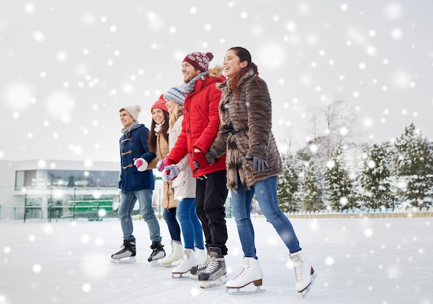 menschen, winter, freundschaft, sport- und freizeitkonzept - glückliche freunde beim eislaufen auf der eisbahn im freien