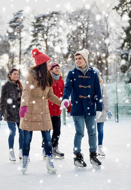 menschen, winter, freundschaft, sport- und freizeitkonzept - glückliche freunde beim eislaufen auf der eisbahn im freien